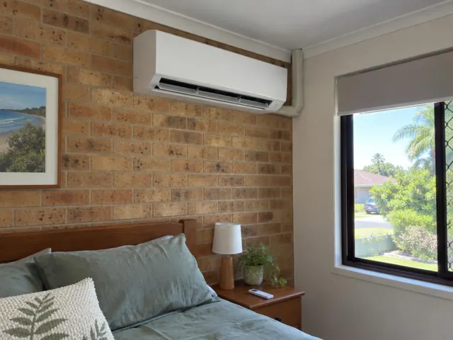 Clean split system mounted high on a brick bedroom wall with louvre open in a home interior in Reedy Creek