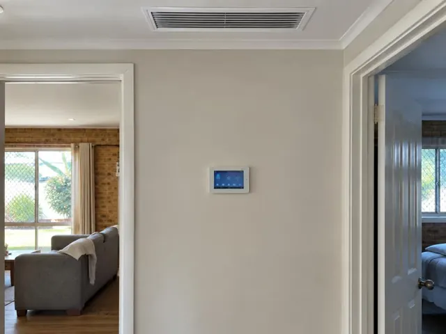 Ceiling return air grille and wall controller in a tidy home hallway with open doorways in Robina