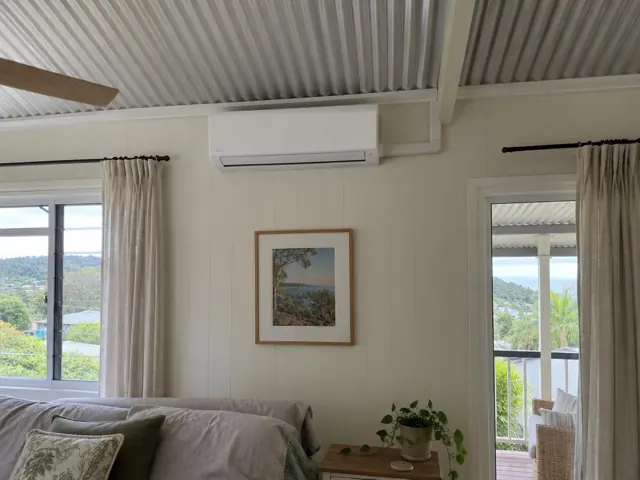 Wall-mounted split system above framed art in a bright living room with curtains in Mudgeeraba